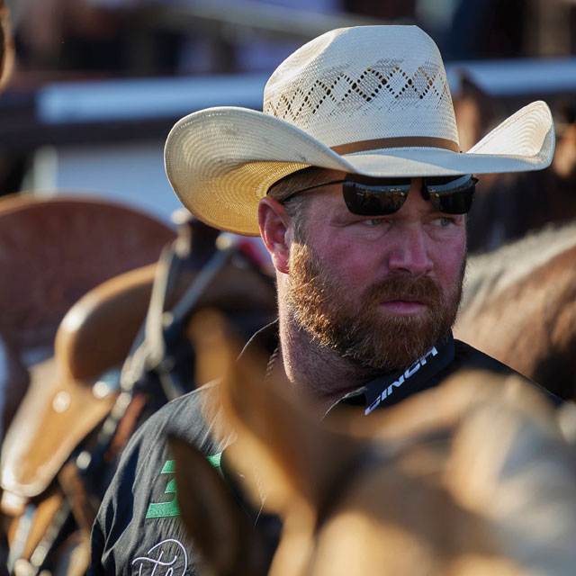 Clayton Hass wearing a straw cowboy hat looking away from the camera by a horse.